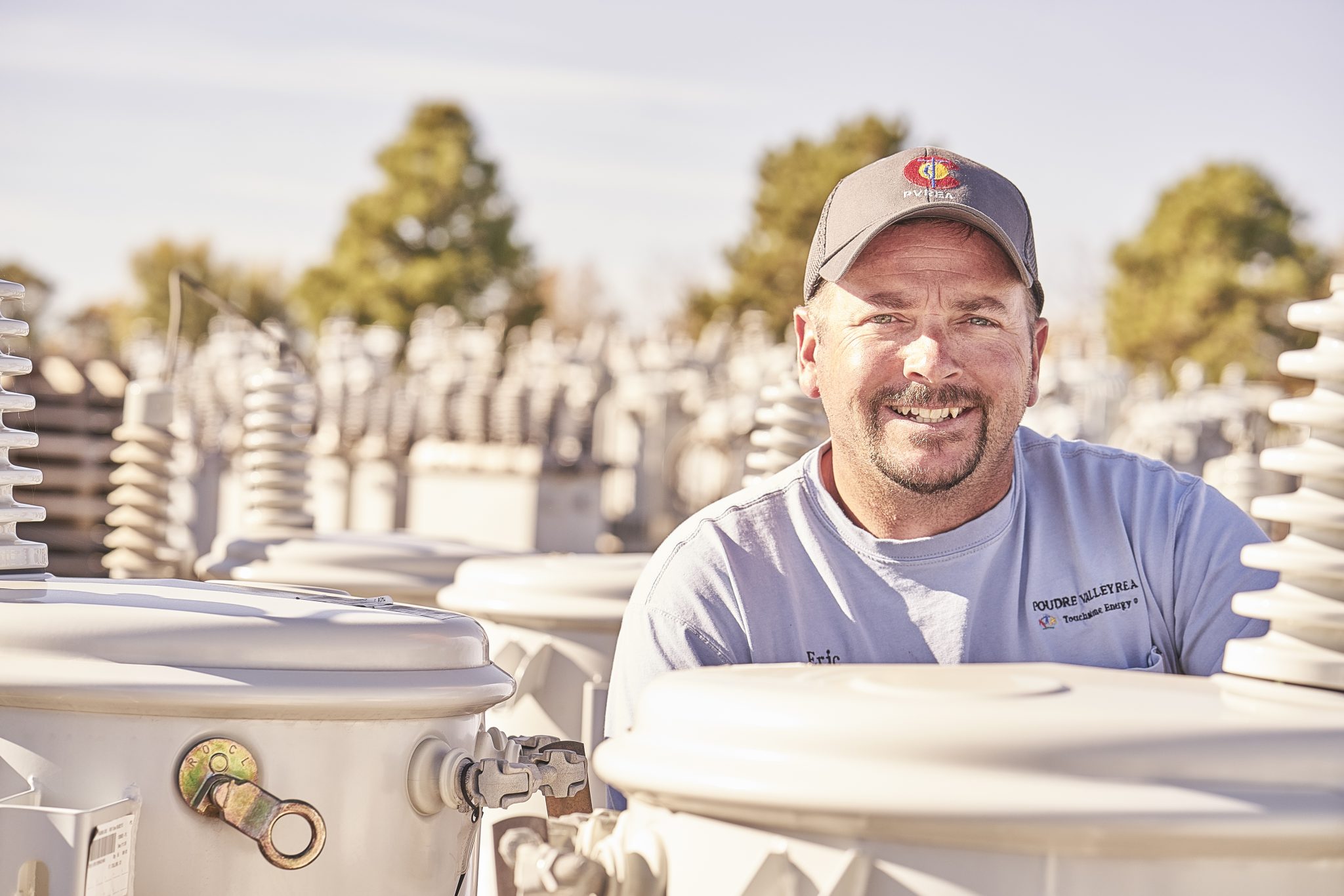 A photo of a co-op employee standing behind electric transformers