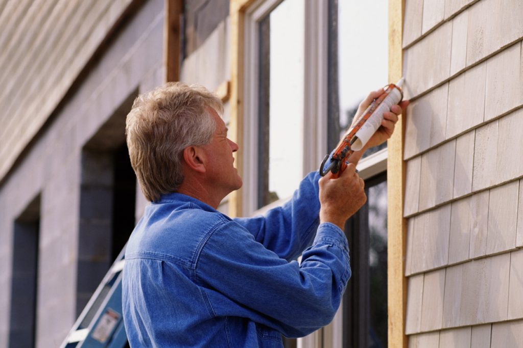 Man applying caulking to an exterior window of a home
