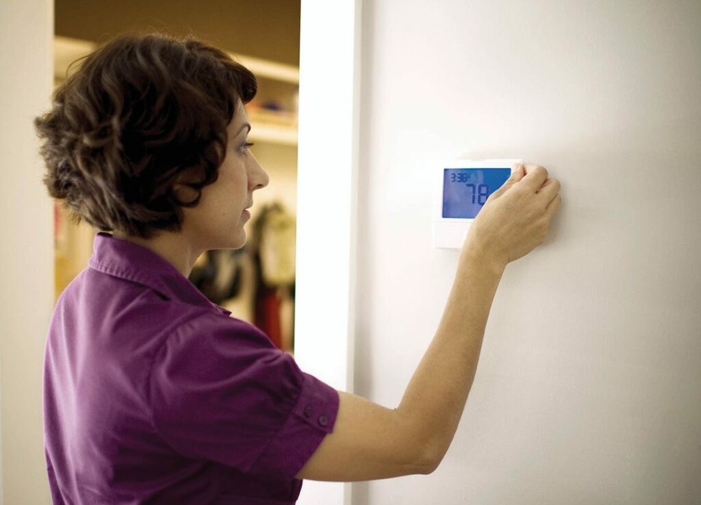 A woman adjusts a thermostat that currently reads 78 degrees Fahrenheit
