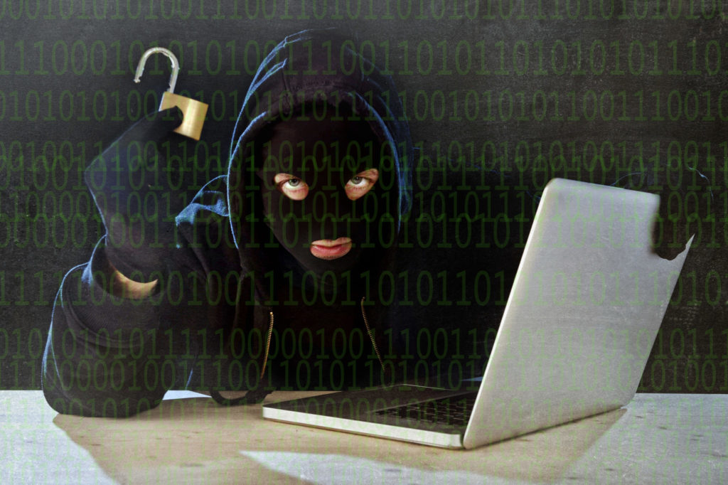 Computer Hacker with a black mask holding an open lock and a laptop