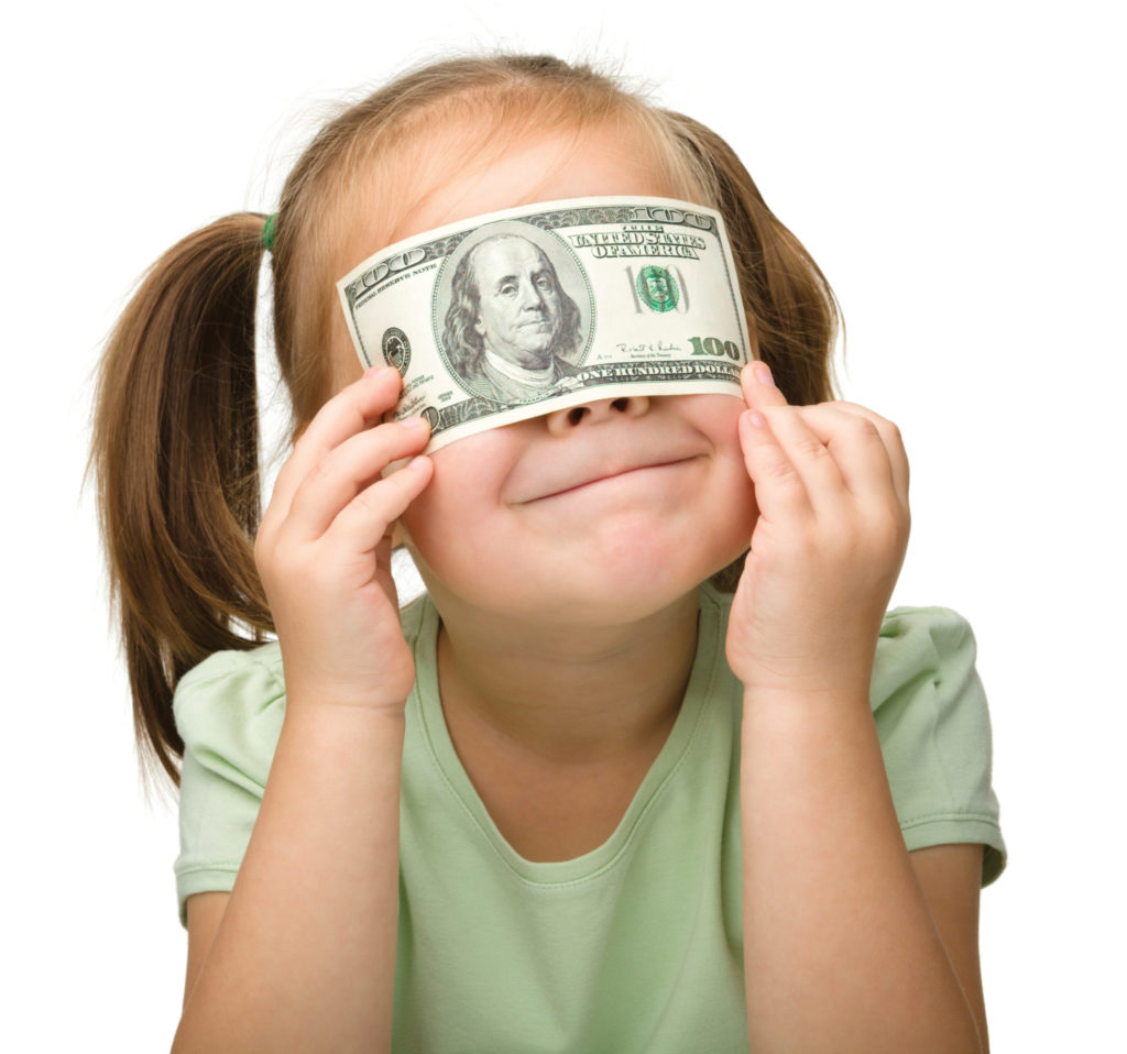 young girl with pursed lips holding a $100 bill over her eyes