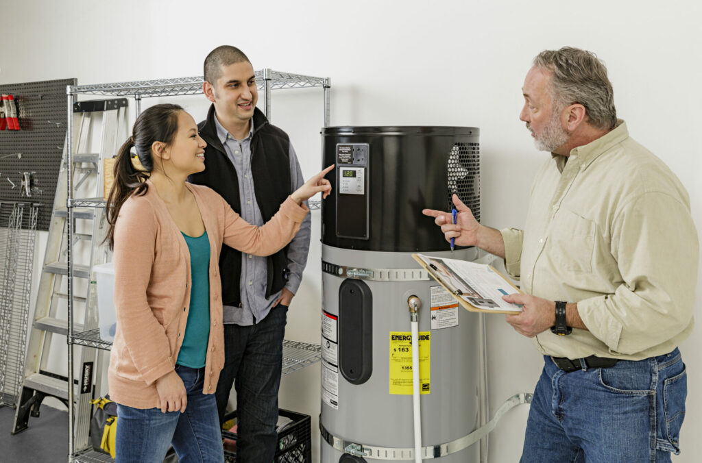 A man and woman look at their heat pump water heater while an installer explain its features