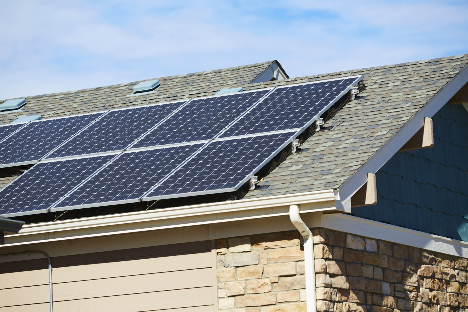zoomed in on solar panels on the roof of a residential home, blue skies with minimal clouds above the house