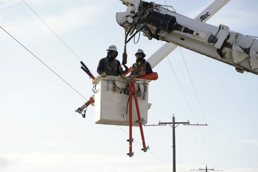 Benton REA lineworkers Kaleb Wentz and Willie Yager prepare to work on high-voltage power lines as they are lifted in a bucket. Photo by David Herder.