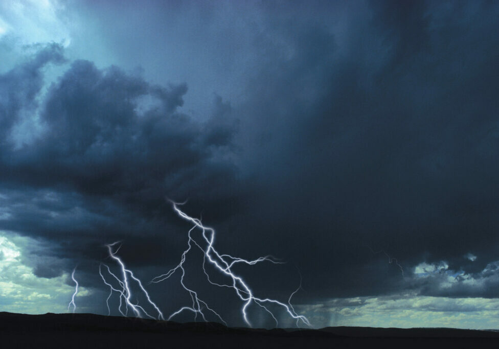 Lightning strikes ground, dark blue clouds hang above. Lightning is the most common cause of a power surge.